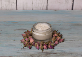 Face cream of roses and vegetable oils in glass jar on a light wooden background. Medicine and natural cosmetics