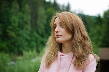 Naklejka premium Attractive young calm blonde woman in pink clothes with long hair on the hill with green forest background during spring or early autumn in the mountains.