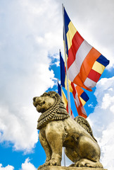 Brave Lion Posture sitting Statue in Gold with Buddhist flags in background