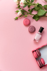 Obraz na płótnie Canvas Flatlay pink coral background, the cup of cappuccino coffee and sweets macaroons, spring white roses, giftbox, beauty stuff - hair pin, nail polish and parfum. Best gift for woman