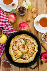 Puff pastry Apple Tart with cinnamon, walnuts and caramel in a pan on a dark wooden background. Rustic style. Vertical orientation. Top view.