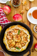 Puff pastry Apple Tart with cinnamon, walnuts and caramel in a pan on a dark wooden background. Rustic style. Vertical orientation. Top view.
