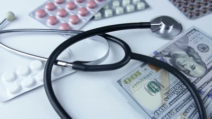 A stethoscope lies on a bundle of money and pills on  a white background. The concept of expensive medicine, medical insurance, expensive drugs.