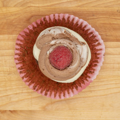 chocolate cupcake with frosting and raspberry garnish on wodden board