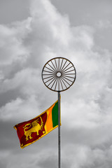 Waving colorful Sri Lankan Lion Flag under the Dharma Chakra symbol in cloudy gray sky background 