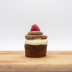 chocolate cupcake with frosting and raspberry garnish on wodden board
