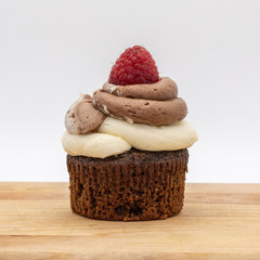 chocolate cupcake with frosting and raspberry garnish on wodden board
