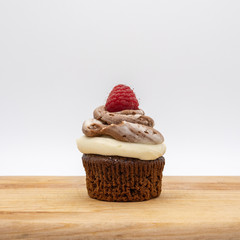 chocolate cupcake with frosting and raspberry garnish on wodden board