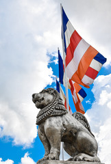 Brave Lion Posture sitting Statue in Silver with Buddhist flags in background