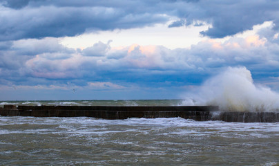 blue stormy clouds, storm at sea, waves are breaking of the pier, dirty orange water