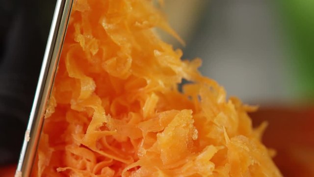 grate fresh carrot on a stainless steel grater, close up