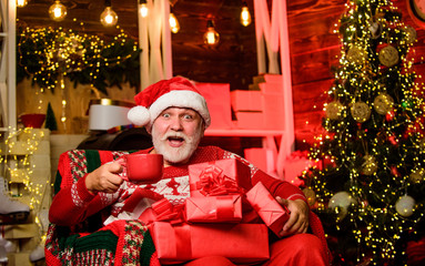 Obraz na płótnie Canvas Delivering gifts. Winter vacation. Elderly grandpa at home. Traditions concept. Santa Claus near christmas tree. Merry christmas. Bearded senior man Santa Claus. Santa Claus relaxing in arm chair