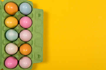 Easter background with a green carton egg box with pastel colored easter eggs in it on a yellow background with space for copy