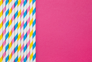 Border of paper straws with stripes against a hot pink background with copy space