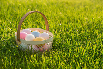 Basket with pastel colored easter eggs on a grass field