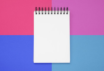 Open notepad on a pink and blue square background. Top view with copy space