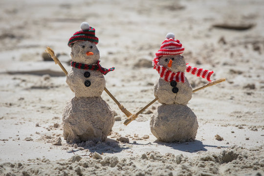 Two Snowmen Made Out Of Sand On The Beach