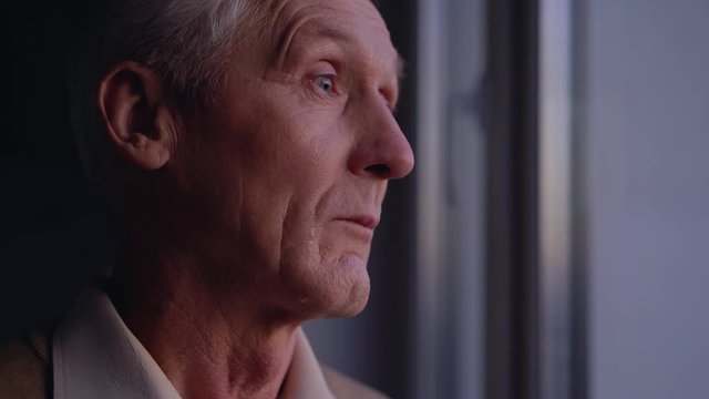 Sad old man crying near window, suffering loneliness, abandoned by relatives