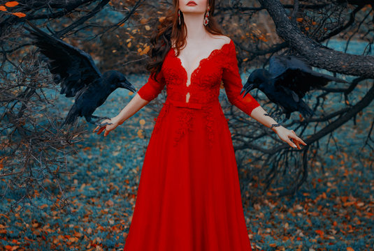 Mysterious woman with red lips in a luxurious dress with a seductive deep neckline. Witch conjures summons black ravens. Glamorous lady with birds. Autumn fairytale landscape. Shooting without a face.