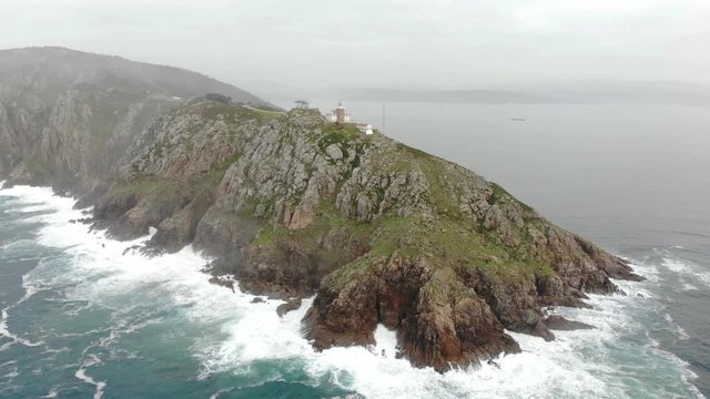 Aerial view of the rocky coast at the Cape at Finisterre in Northern Spain in Galicia. In the middle is the famous lighthouse. There is a lot of haze in the air and there are high waves.