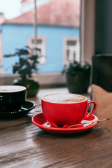 Red and black ceramic cups of cappuccino on wooden table inn a cafe. Mockup for your design. Close-up.