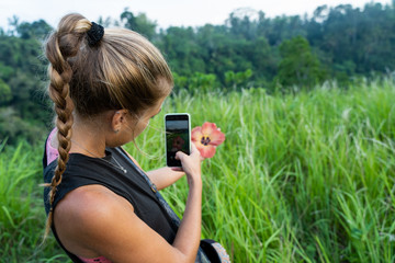Woman taking a picture with her mobile phone of a flower she is holding in her hand