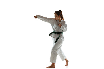 Confident junior in kimono practicing hand-to-hand combat, martial arts. Young female mongol fighter with green belt training on white studio background. Concept of healthy lifestyle, sport, action.