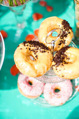 Candy bar with donuts on a stand. Decorative sweet wedding table in bright colors of blue, turquoise and pink. Decorated with lanterns, pillows, upholstered furniture, watches and flowers.