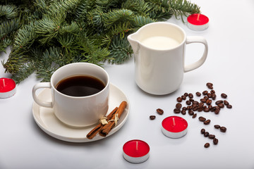 Cup of espresso with milk, cinnomon sticks, fir trees, red candles and on a white background. View from above. Selective focus.