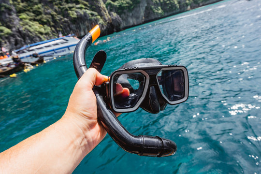 Hand holding snorkeling mask and pipe over ocean water. Summer holiday background.