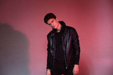 Cute brutal man in black leather jacket model style. Portrait of a handsome guy on pink studio background. Man In Black Jacket. Young Fashion Man In Leather Jacket on a pink background