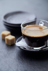 Coffee in glass cup and two brown sugar cubes on dark stone background. Close up.