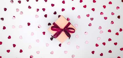 Craft box with dark red velvet ribbon bow and glitter heart confetti. Valentine day and eco-friendly wrapping concept. Trendy minimalistic flat lay design background. Wide screen banner format