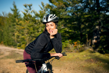 Cute young female cyclist with bike in nature environment