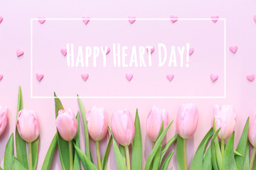 Happy Heart Day wording with pink tulips and pink heart sprinkles on the pink background. Flat lay, top view. Valentines background. Horizontal
