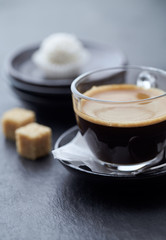 Coffee in glass cup and two brown sugar cubes on dark stone background. Close up.
