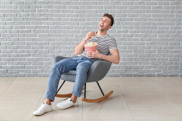 Happy man watching movie while sitting in armchair near grey wall