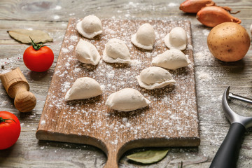 Board with raw dumplings and ingredients on wooden background