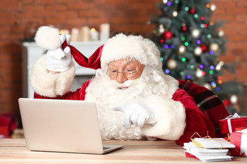 Santa Claus with laptop checking his mail in room decorated for Christmas
