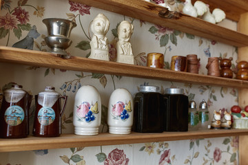 Variety of vintage salt and pepper shakers on a wooden shelf against floral wallpaper.  Maine, USA