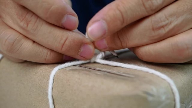 Close up of Woman hands wrapped a gift box by brown recycled paper and tied sack rope for party.