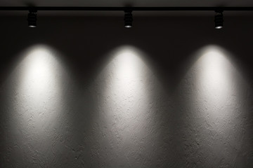 White wall with track light. Spotlight beams on the wall. Dark background.