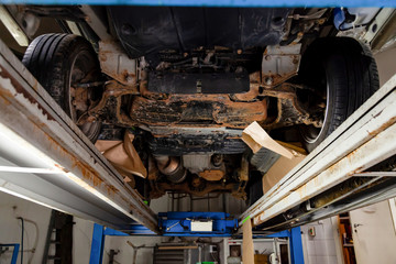 The bottom of the car lifted on a lift covered with brown and orange rust during anti-corrosion...