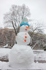 Cheerful snowman with carrot nose and blue bucket on his head in winter snowy park. Bottom view. Snowman in the snow