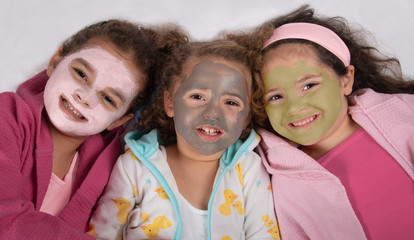 Smiling, mixed race sisters in bathrobes and pink, gray and green facial masks - Powered by Adobe