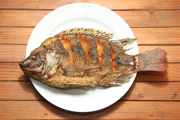 Fried tilapia fish on white plate on wooden background.