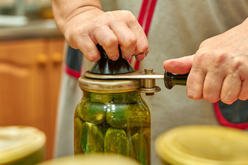 Preservation of fresh house cucumbers in glass jars using seamer. Closeup, selective focus