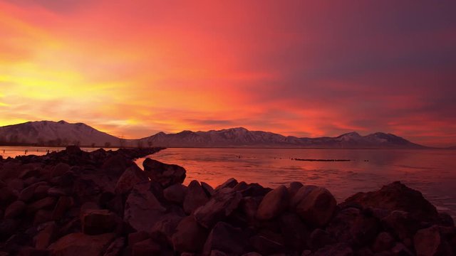 Panning view of sunrise landscape as the sky looks on fire and ice covers Utah Lake during winter.