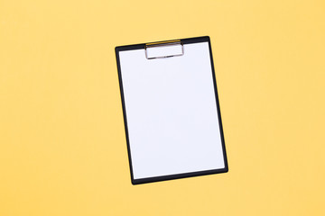 Clipboard with white sheet and pen on a yellow background. View from above. space for text