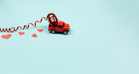 Fototapeta premium Valentines Day Theme Concept. Retro red toy car with red carnival serpentine and red heart confetti on mint background. Copy Space.